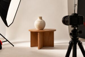 Set di fotografia prodotto con vaso in ceramica su tavolino in legno, softbox e fotocamera su treppiede, senza persone.